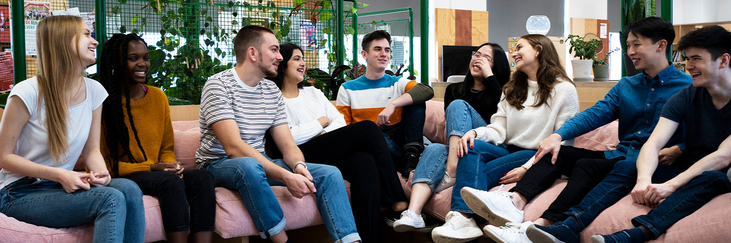 A diverse group of young people talking together and smiling in a student common room